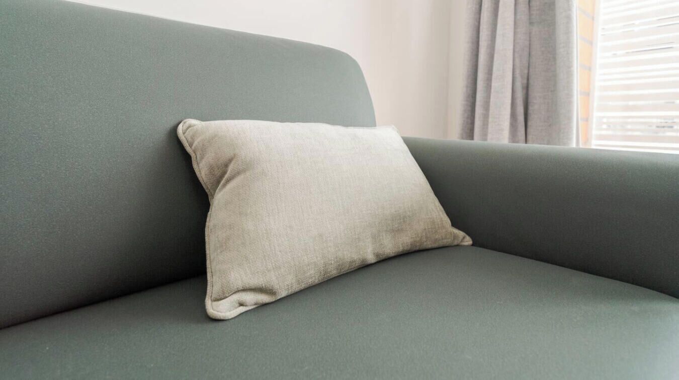 A green sofa with a beige pillow.
