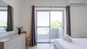 A modern bedroom with a bed, a dresser, a chair, and a balcony with curtains.