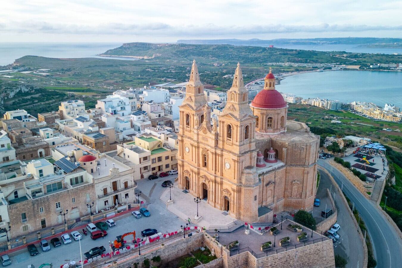 Una iglesia histórica con una cúpula destacada y dos torres gemelas, rodeada de edificios residenciales y vistas al mar.