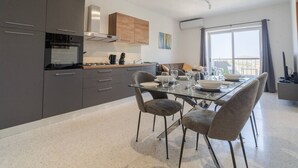 A modern kitchen with dark cabinets, a glass dining table, and a view of the outdoors.