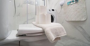 A bathroom with a marble wall, a washing machine, and a towel rack with a folded towel.