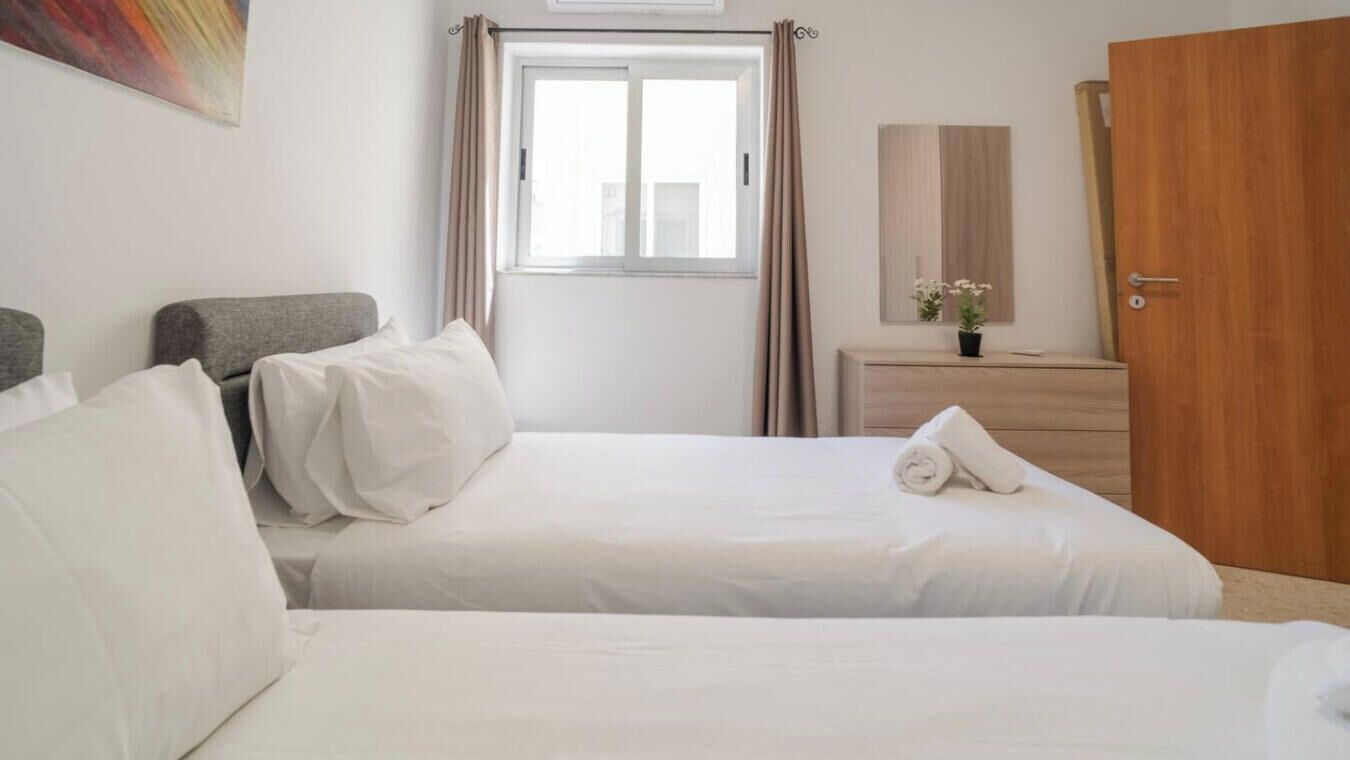 A hotel room with two beds, a window with curtains, a wooden dresser, and a painting on the wall.