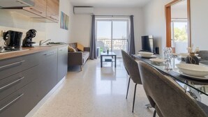 A modern kitchen with a dining area, a sofa, and a view of the outdoors.