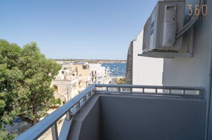Een balkon met uitzicht op een kustplaatsje, een heldere lucht en een gebouw met een airconditioning.