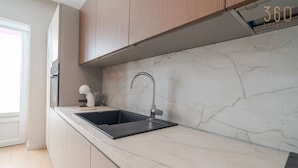 Eine moderne Küche mit Marmorarbeitsplatte, Spüle aus Edelstahl und Holzschränken.