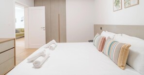 A modern hotel room with a bed, a wardrobe, and a door leading to another room.