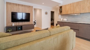 Una sala de estar moderna con televisor de pantalla plana, un sofá y una zona de cocina con armarios de madera y encimera de mármol.