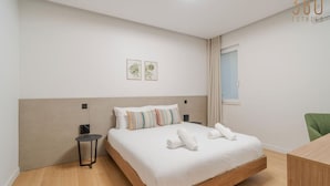 Una habitación de hotel moderna con una cama de madera, una mesita auxiliar y una silla verde.