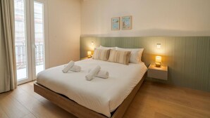 Een hotelkamer met een groot bed, twee nachtkastjes met lampen, uitzicht door een schuifdeur en een muur met twee ingelijste foto’s.