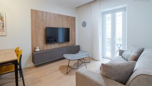 Een moderne woonkamer met een flatscreen televisie, een grijze bank, een klein rond tafeltje en een houten accentmuur.