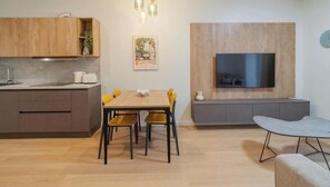 A modern kitchen with wooden cabinets, a dining area with yellow chairs, and a TV mounted on a wooden wall.