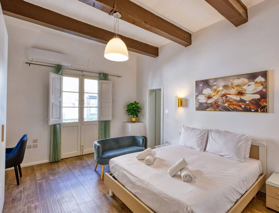 A bedroom with a bed, bedside tables, a chair, a window, and a painting on the wall.