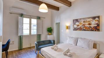 A bedroom with a bed, bedside tables, a chair, a window, and a painting on the wall.