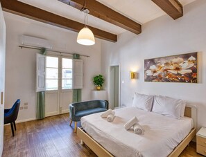 Une chambre à coucher avec un lit, des tables de chevet, une chaise, une fenêtre et un tableau au mur.
