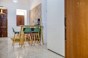 A hallway with a wooden door, a green chair, a table with a coffee machine, and a patterned wall. - Fully equipped Cozy Home in Bormla w/ WIFI & AC (Cospicua)