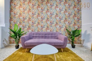A room with a purple sofa, a white coffee table, and a patterned wallpaper. There are two potted plants on either side of the sofa. - Fully equipped Cozy Home in Bormla w/ WIFI & AC (Cospicua)