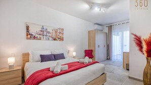 A modern hotel room with a large bed, a red throw blanket, and a cityscape painting on the wall.