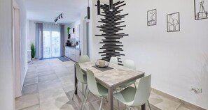 Uma área de jantar moderna com mesa minimalista, cadeiras em tons claros e um painel decorativo na parede.