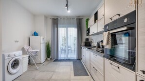 A compact kitchen with a washing machine, a dining area with a chair, and a view through a glass door.