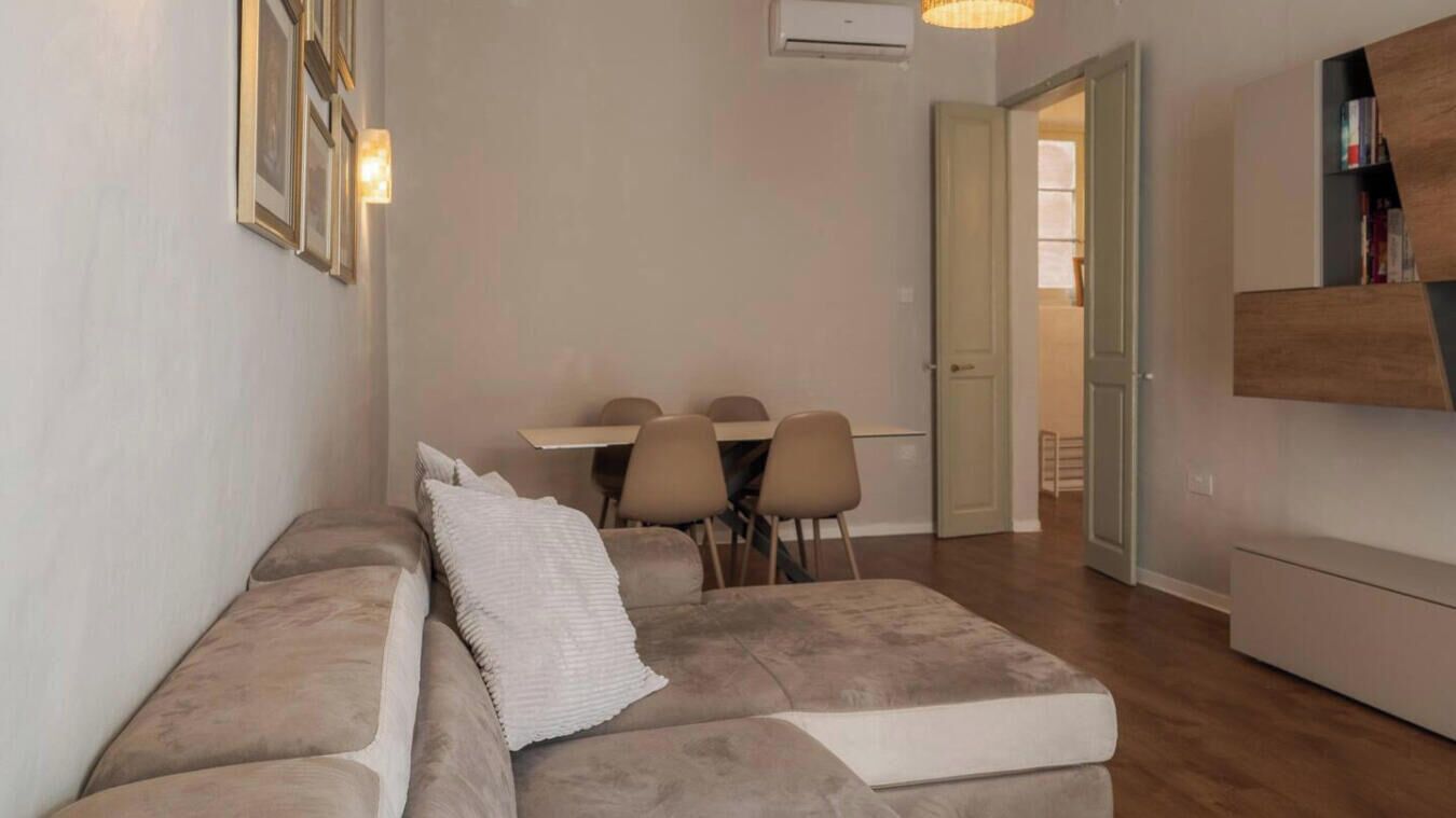 Ett modernt vardagsrum med en soffa, ett matbord med stolar och en hängande lampa.