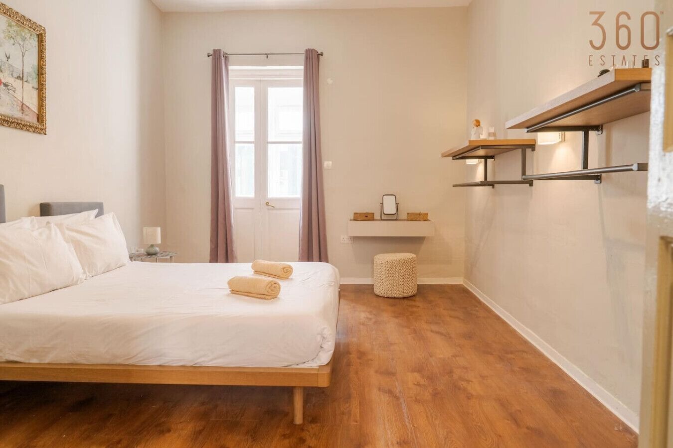 Een slaapkamer met een bed, nachtkastje, raam met gordijnen, een klein krukje en een plank met spullen.