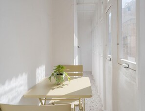 A narrow corridor with a table and chairs, a potted plant, and a door leading to an outdoor area.