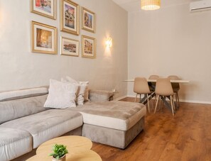 A modern living room with a grey sectional sofa, a dining table with chairs, and framed pictures on the wall.