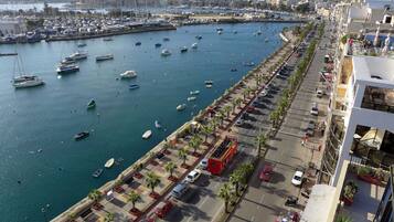 A marina with numerous boats docked, a parking area with cars, and a row of buildings along the waterfront.