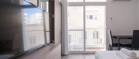 Une chambre d’hôtel équipée d’un lit, d’un bureau, d’une chaise, d’une télévision et d’un balcon offrant une vue sur les bâtiments.