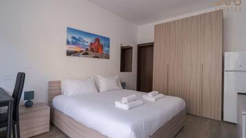 Moderni hotellihuone, jossa on suuri sänky, työpöytä ja vaatekaappi.