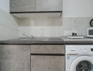 Una cocina compacta equipada con lavadora integrada, microondas y fregadero.