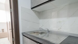 Eine moderne Küche mit Spüle aus Edelstahl, grauen Arbeitsplatten und einer weißen Marmor-Spritzschutzwand.