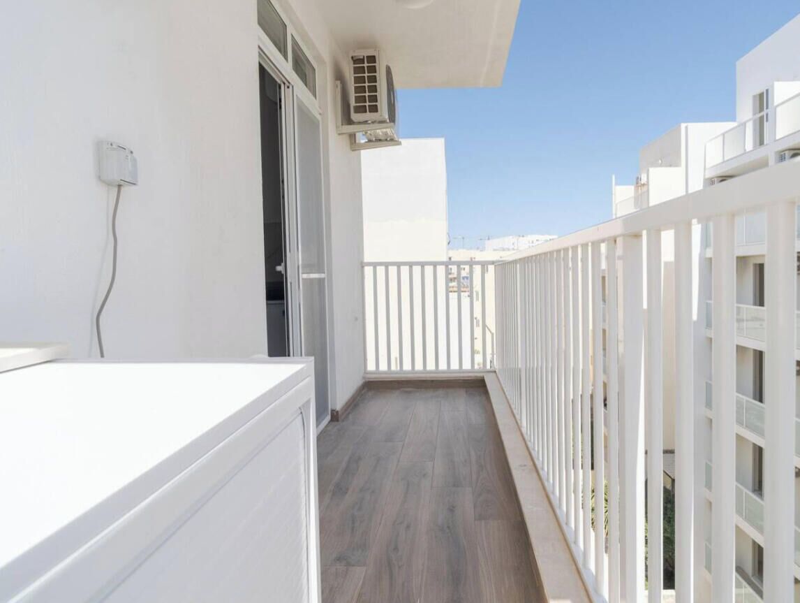 A narrow balcony with a wooden floor, white railings, and a white wall.