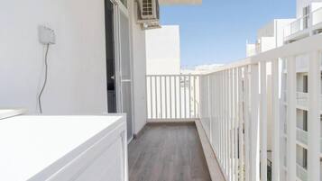 A narrow balcony with a wooden floor, white railings, and a white wall.