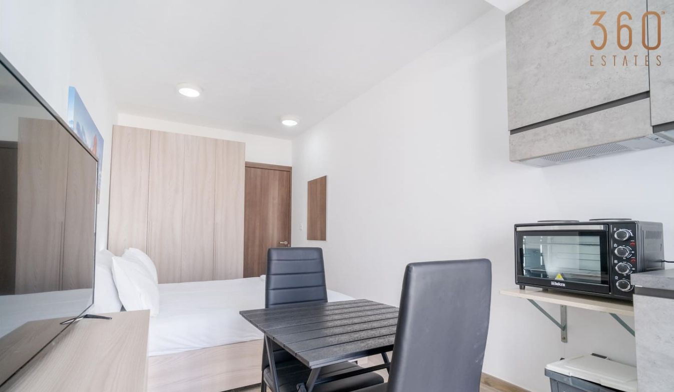 Una habitación de hotel moderna con una cama, un escritorio, una silla, un microondas y un cesto de basura.