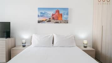Una habitación de hotel con una cama, dos mesitas de noche con lámparas, un televisor en un mueble y un cuadro de un castillo en la pared.