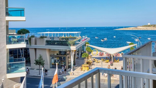 Um edifício moderno com várias varandas com vista para uma área costeira com barcos e céu claro.