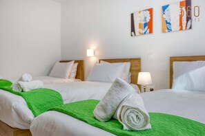 A hotel room with two beds, each with a green quilt and white bedding. There are two wall-mounted lamps and a painting above the beds.
