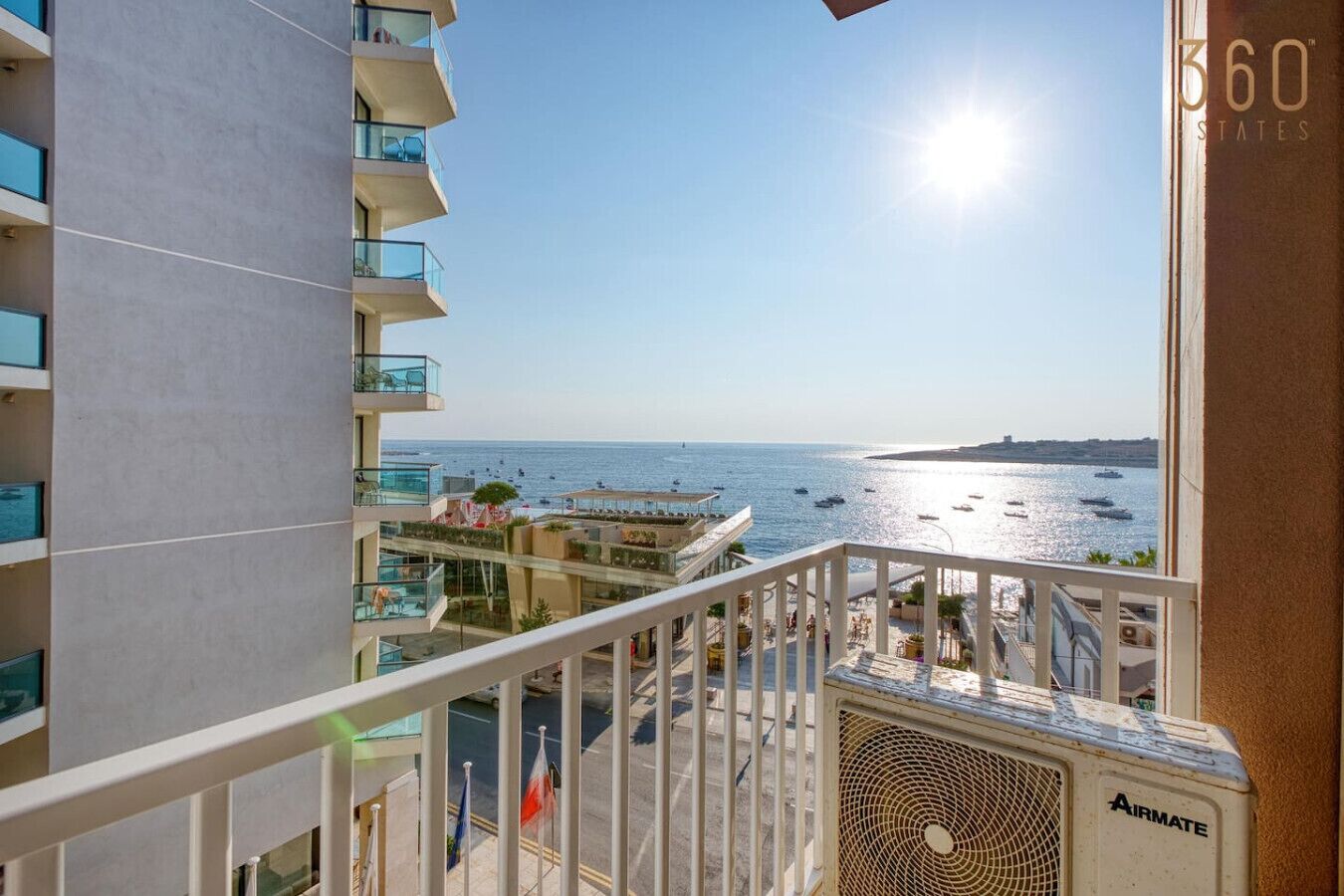 Un balcon donnant sur la mer et les bateaux, un ciel dégagé et un immeuble doté de balcons.