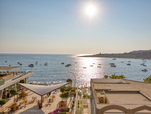 A coastal view with a marina, outdoor seating, and a clear sky. - Seafront home, opposite beach w/WIFI & AC in Qawra (St. Paul`s Bay)