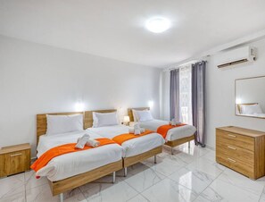 A modern hotel room with two beds, a wooden dresser, a mirror, and a ceiling light. - Seafront home, opposite beach w/WIFI & AC in Qawra (St. Paul`s Bay)
