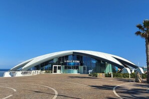 Edifici modern de disseny corbat amb façana de vidre i la inscripció 'LA NAVE BISTRO' al frontal.