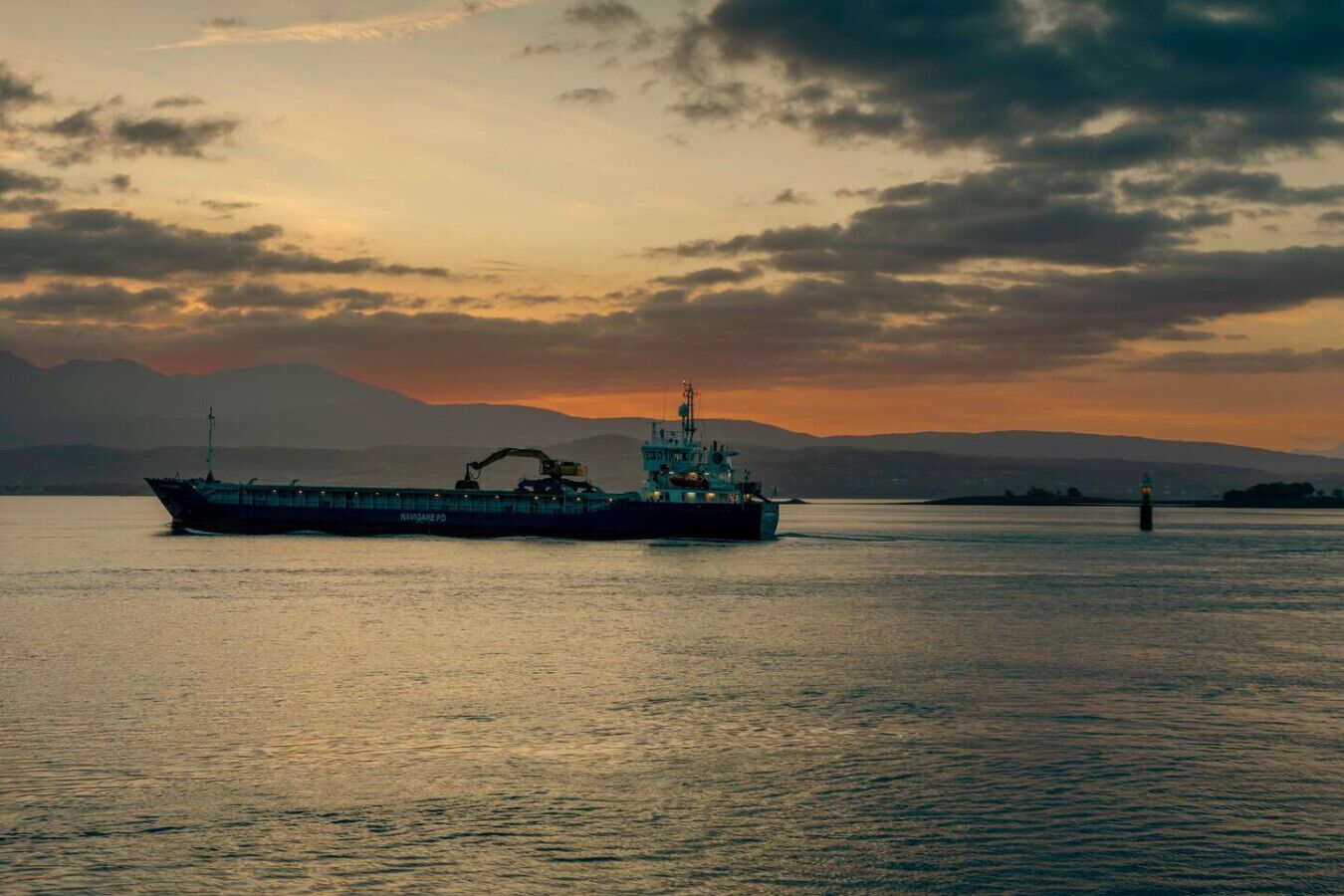 Ein großes Frachtschiff auf ruhigem Wasser vor einer gebirgigen Kulisse.