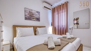A hotel room with a large bed, a painting of a ship on the wall, a mirror, and a sign reading "360 ESTATES".