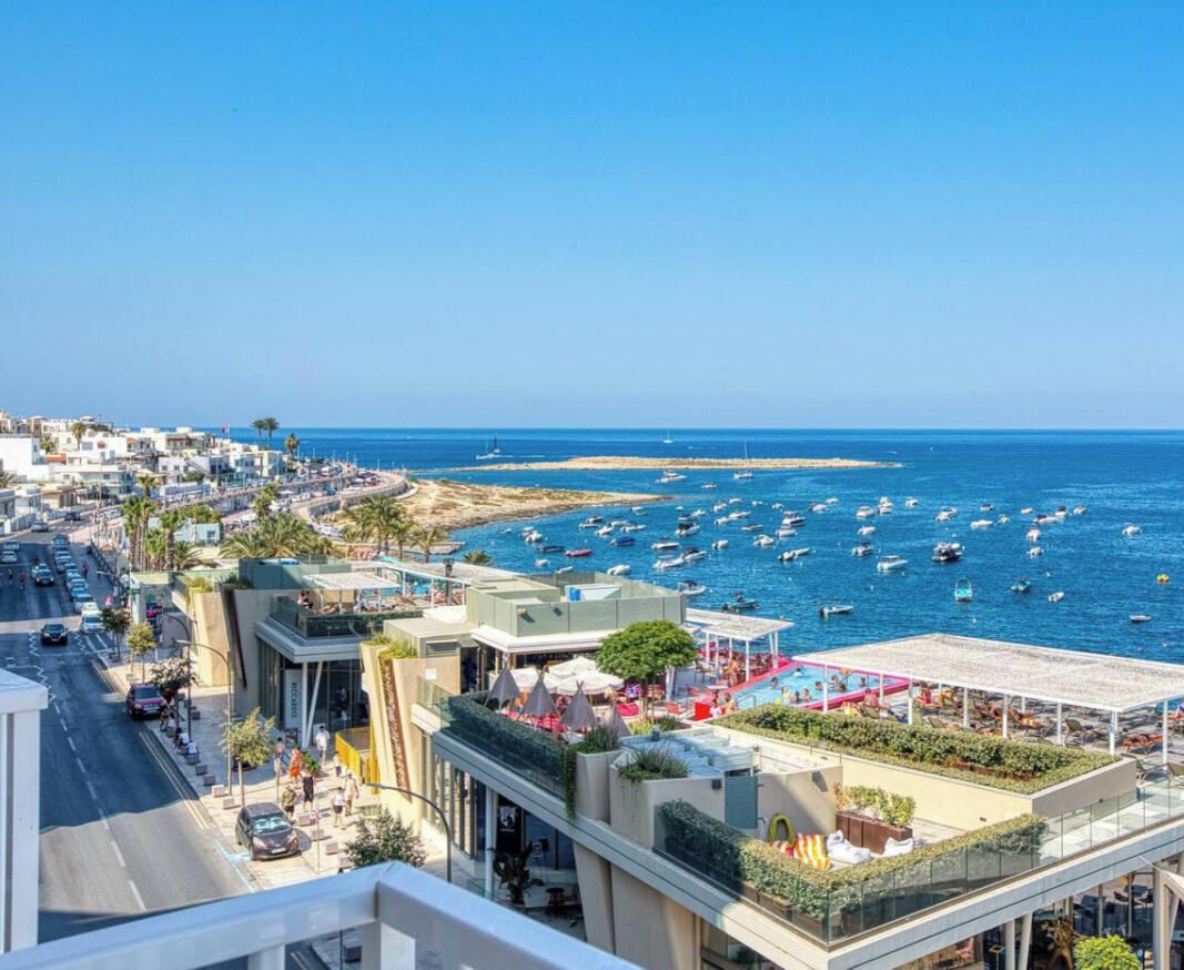 A coastal cityscape with a marina, buildings, and a clear sky.