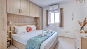 A bedroom with a bed, wooden wardrobe, and an air conditioning unit. - Stylish 2BR Stay with Balcony Sunsets & Sea Views! (St. Paul`s Bay)