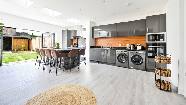 A modern kitchen with built-in appliances, a dining area with a round table and chairs, and a laundry area with washing machines.