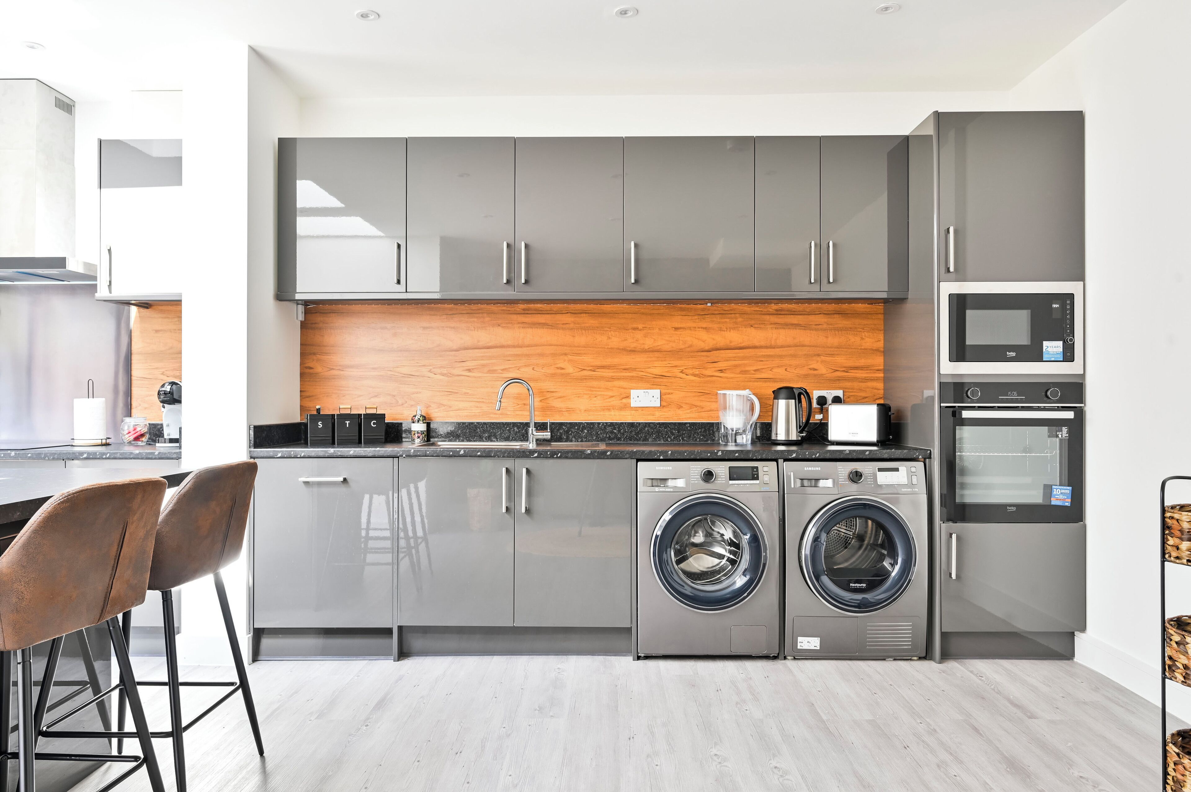 A modern kitchen with grey cabinets, a wooden backsplash, a built-in washing machine, and a microwave.