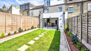 A residential backyard with a lawn, stepping stones, a wooden fence, and a house with a modern design.