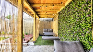 An outdoor patio with a wooden ceiling, string lights, a bench, and a wall covered in greenery.